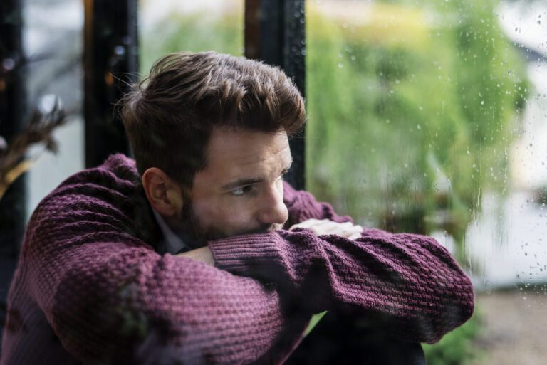 Adult with ADHD and depression sitting by a rainy window.