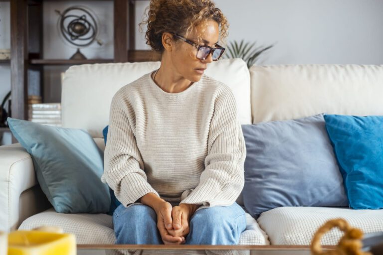 Middle-aged woman alone on sofa with sad expression, symbolizing adult ADHD, depression, and anxiety.